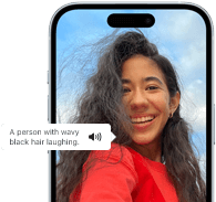 iPhone 15 s aktivní funkcí Voiceover, která popisuje obrázek smějící se osoby s vlnitými černými vlasy